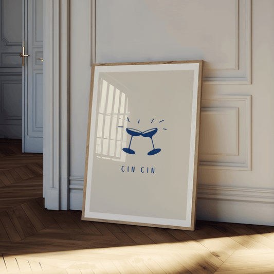 Two champagne coupe's toasting, cheersing, clinking each other in navy against a neutral cream-beige background with the typography "cin cin", print is framed leaning against a wall