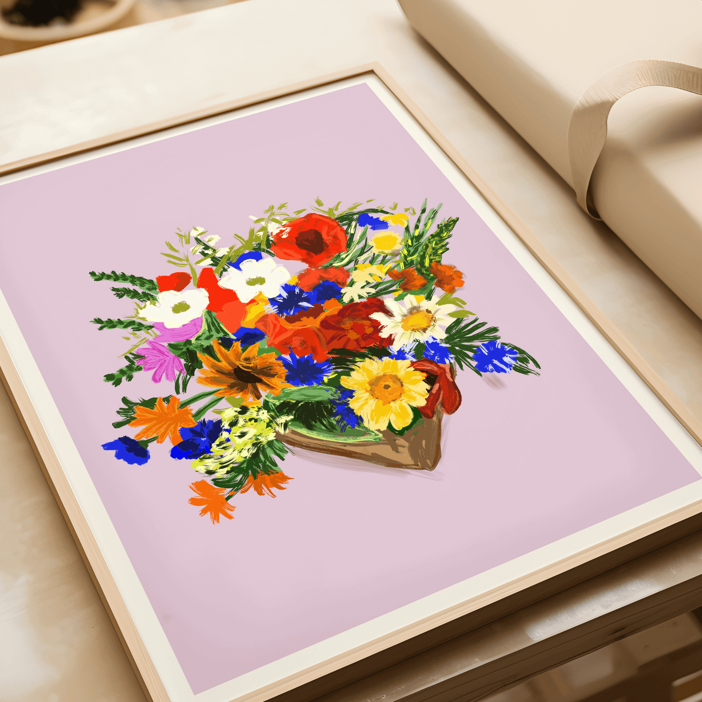 Print features a bouquet of colourful bouquet of flowers, against a dusty pink/lilac background with a small white border. The bouquet features yellows, blues, reds, whites and green foliage. Displayed in a light wood frame, laying flat.