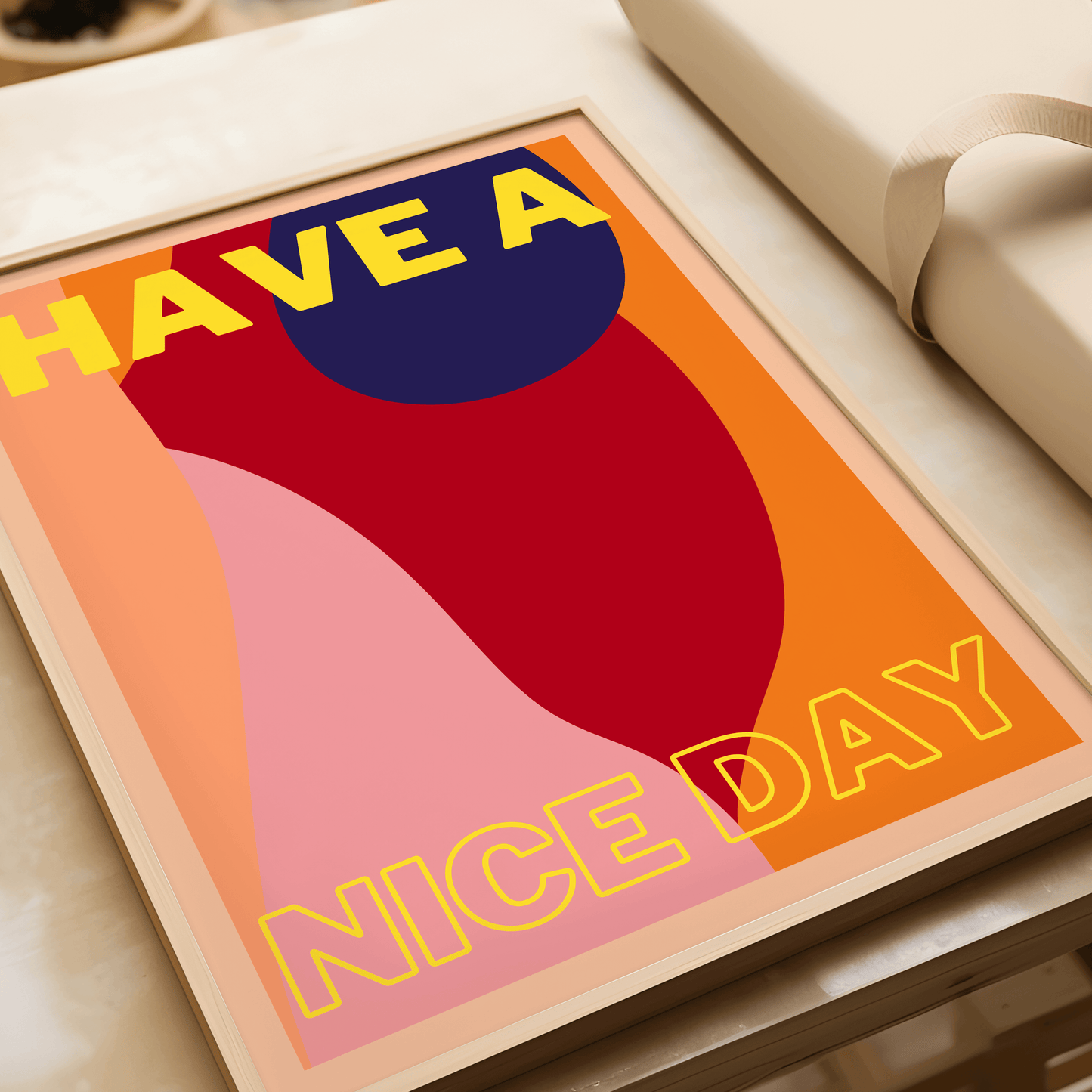 Print features block typography saying "Have a nice day". The background features abstract shapes and a variety of complimentary red, navy, peach and orange shades. The typography is yellow for a statement look. Displayed in a light wood frame, laying fla