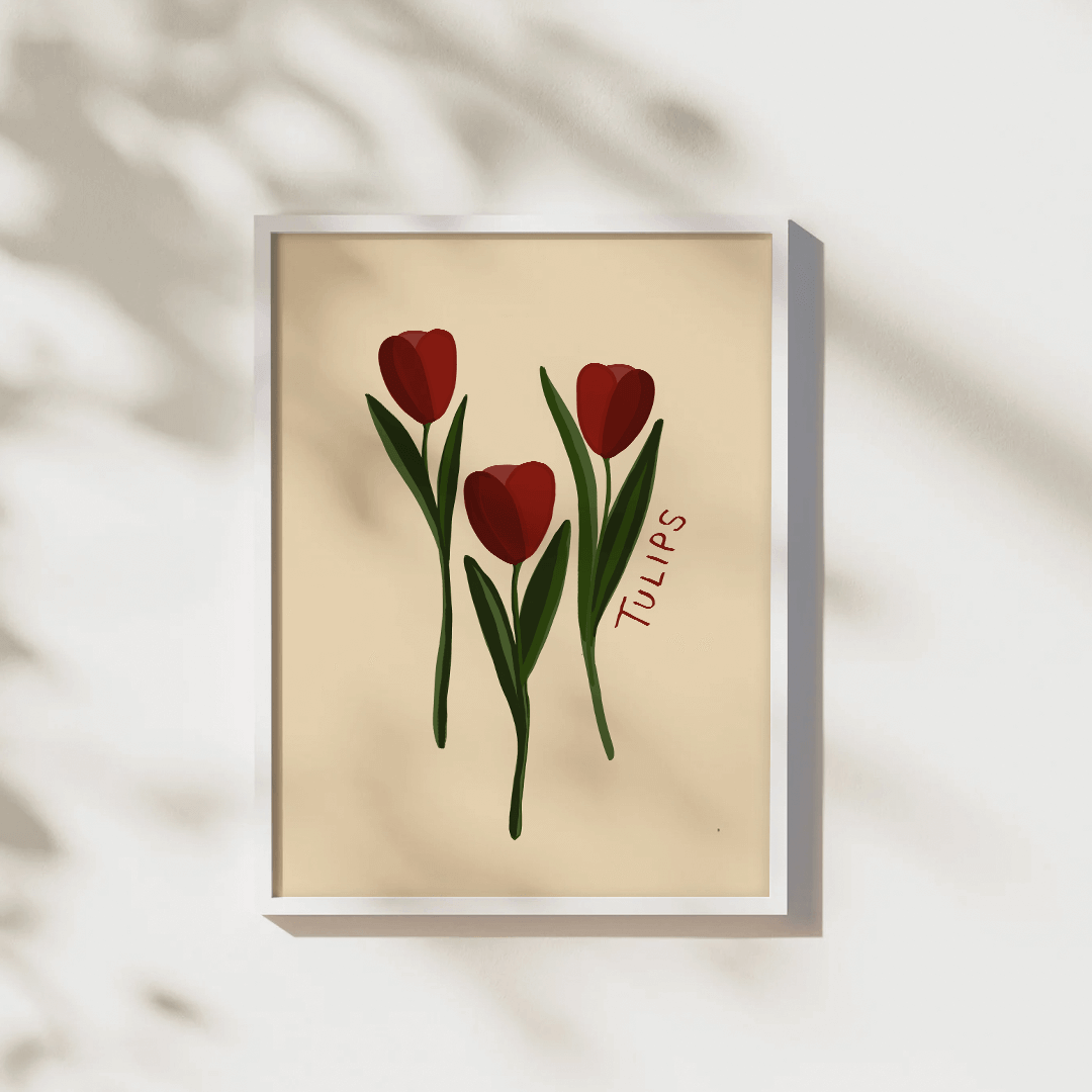 Simplistic print of three red tulips, with green stems against a beige background. Displayed in a white frame on a wall with tree shadows.